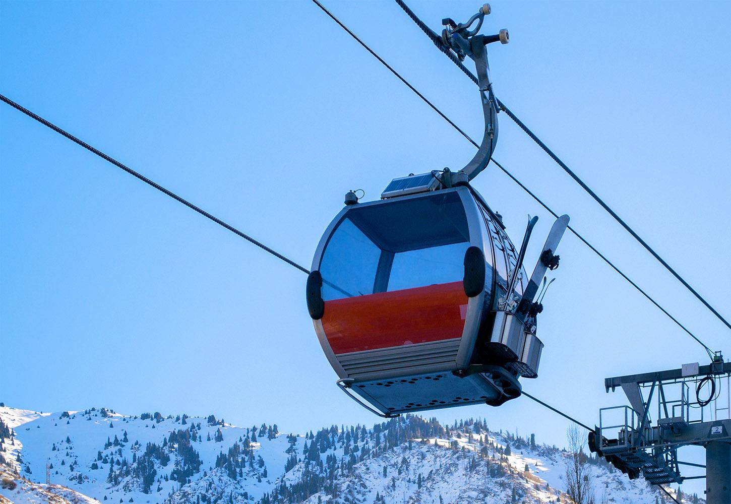 Gondola,Of,Ski,Lift,Above,Snow,Capped,Mountains,Against,Blue
